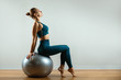 © Georgii - Fitness girl with fitball on in the gym room on gray background. Kinky body, flexibility and stretching. Copy space