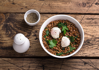 Boiled lentils with spinach, herbs, spices and poached egg in ceramic bowls on a wooden background. Simple healthy homemade food	