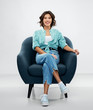 © Syda Productions - comfort, people and furniture concept - portrait of happy smiling young woman in turquoise shirt and jeans sitting in modern armchair over grey background