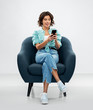 © Syda Productions - people and technology concept - portrait of happy smiling young woman in turquoise shirt and jeans with smartphone sitting in modern armchair over grey background