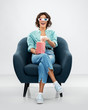 © Syda Productions - comfort, people and furniture concept - portrait of happy smiling young woman in 3d movie glasses eating popcorn from striped bucket sitting in modern armchair over grey background