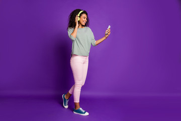 Sticker - Full length profile side photo of positive teen afro american break pause use smart phone browse popular songs wear headset listen music have pink trousers isolated violet color background