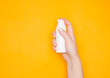 A woman's hand with a white plastic bottle with a pump. Care cosmetics, antiseptic. Yellow background.
