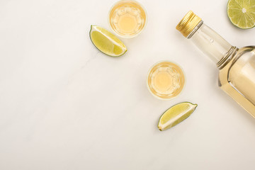 Sticker - top view of golden tequila in bottle and shot glasses with lime on white marble surface