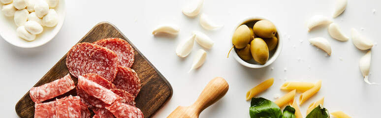 Wall Mural - Panoramic orientation of meat platter, rolling pin, pasta, garlic and bowls with olives and mozzarella on white background