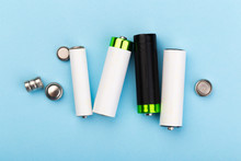 Many New And Used Batteries Of Different Shapes, AA, Round Batteries On A Blue Background.