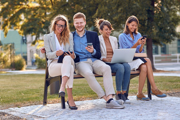 Wall Mural - Smiling Business people on bench at park,working on laptop,texting message.