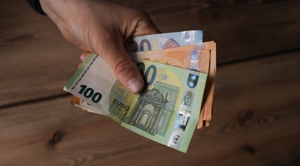 Canvas Print - Hands of a man holding European Euro bills with the wooden table in the background