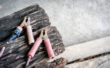 Old dirty rusty jumper cable for charging a car battery on a wooden table with a concrete background, and there is a copy space to put text on the right. Vintage style photo and abstract concept