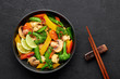Pad Pak Ruam or Veg Thai Stir-Fried Vegetables in black bowl on dark slate backdrop. Pad Pak is thailand cuisine vegetarian dish with mix of vegetables and sauces. Thai Food. Top view