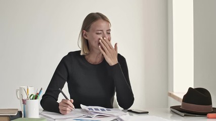 Poster - An attractive young blonde businesswoman is yawning while finishing her working day and do away from a white office