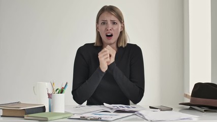 Poster - A shocked frightened young blonde woman is worried about something while sitting at the table indoors in a white office