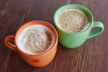 Two cups of fragrant cappuccino on a wooden roofing paper. Airy milk foam of a hot drink. Coffee drink with milk