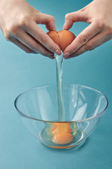 Women's hands smashed a breakfast egg into a glass bowl. The yolk is inside the cup. Step by step an omelet. Step 2