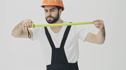 Sticker - Concentrated young bearded man builder isolated over white wall background in helmet holding centimeter