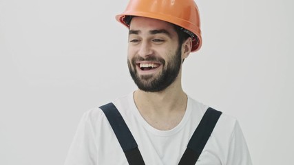 Sticker - Pleased positive optimistic young bearded man builder isolated over white wall background in helmet with brush