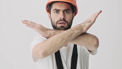 Sticker - Handsome angry serious young bearded man builder isolated over white wall background in helmet make stop gesture