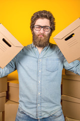 Wall Mural - Portrait of a delivery man holding two cardboard boxes on his shoulders on a yellow background, vertical photo