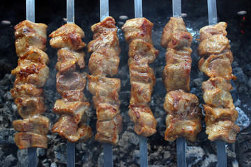 Tasty pork shish kebab on skewers roasting on hot smoky charcoal