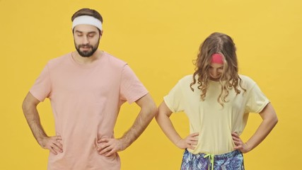 Sticker - A smiling young athletic couple man and woman in sportswear are warming-up exercises together isolated over a yellow background in studio