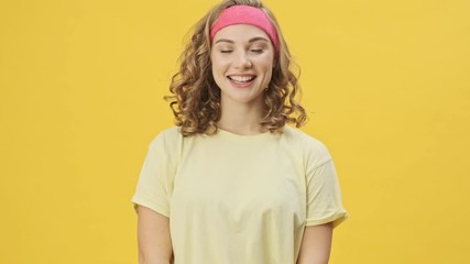 Sticker - A beautiful young athletic woman in sportswear is smiling isolated over a yellow background in studio