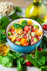 Wall Mural - Concept of healthy food, clean eating, low calories delicious meal. Salad with quinoa and fresh vegetables with olive oil in blue bowl. Ripe tomato, avocado, spinach. Close up, wooden background