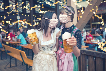 two women in dirndl, traditional fashion with mask on okoberfest