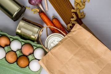 eggs in a box, canned food, macaroni, spaghetti on a gray background form a grocery basket, essential food,