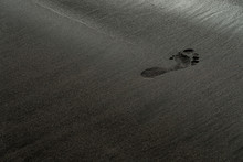 Footprint on a black sand beach macro photography. Human trace on a silky black beach texture with shallow depth of field. Minimalistic black background. Tenerife voulcanic sandy shore.