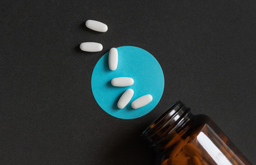 Wall Mural - White tablets pills spilling out of a toppled brown bottle over dark background