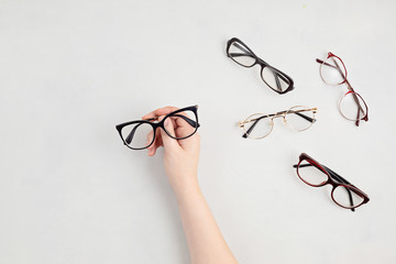 Sticker - Woman hand holding eyeglasses. Optical store, glasses selection, eye test, vision examination at optician, fashion accessories concept. Top view