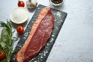 Raw meat with rosemary, spices and tomatoes on a black slate on a light background. Top view. Copy space