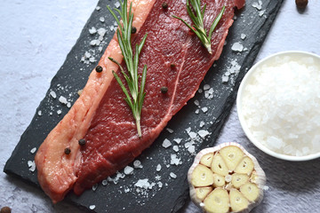 Raw meat with rosemary, peppercorns on a black slate on a light background.