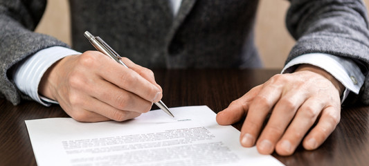 a businessman sits at an office desk and signs a contract with a ballpoint pen