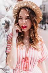 Wall Mural - Fascinating girl in retro straw hat posing on city background. Outdoor photo of elegant caucasian woman in striped dress standing near disco balls.