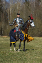 Young Adult Man In Knightly Armor Rides Across The Field On A Horse In Armor