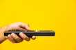 © Nopphon - Close up male hand holding television remote control on isolated yellow background.