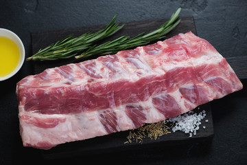 Wall Mural - Closeup of raw fresh pork ribs with seasonings on a black wooden chopping board, horizontal shot