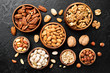Mix of nuts in wooden bowls on black stone background. Walnuts,  almond, pistachio, pecan, hazelnut, pine nut. Healthy various super food selection.