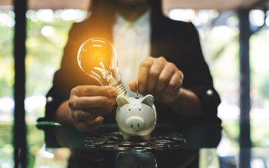 A businesswoman putting coins and a light bulb over piggy bank for saving money concept