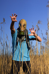 Man in gas mask crouching through the field with hand in blood. Guy in blue t shirt and scarf Shemagh. Concept of infection, apocalypse and pollution. Hope concept. Anti virus mask.