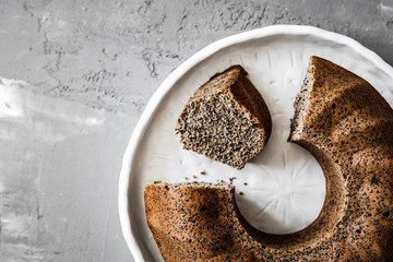 Canvas Print - A close-up of a poppy seed bundt cake on white ceramic plate on grey background, top view photo