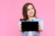 © Monstar Studio - Pretty smiling girl is holding in hands tablet computer with empty blank screen display. Young woman dressed in denim jacket and white t-shirt on pink background. Modern technology and devices concept