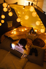 Wall Mural - little 11 year old girl using laptop under her home-made tent inside the living room.