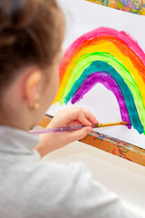 Wall Mural - Child is drawing rainbow with watercolors on the sheet of paper on the easel. Creativity concept.