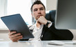 © ANR Production - Young successful businessman and office employee reading news on his tablet. Coffee break during the working day. A financial analyst or broker studies stock market fluctuations. Economic crisis 2020