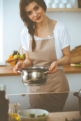 Wall Mural - Young brunette woman cooking soup in kitchen. Food and health concept