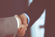 © rogerphoto - Business people shaking hands while standing with colleagues after meeting or negotiation, close-up. Group of unknown businessmen and women in modern office. Teamwork, partnership and handshake