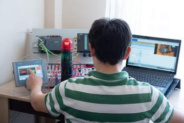 Back View of Young Man Who is Working Home Office and Making Online Education about PLC and Operator Panel Programming. Distance learning, also called distance education, e-learning or online learning
