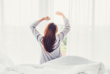 Happy young woman relaxing and stretching body in the morning with opening window curtains at home. Concept of people ready to start day with fresh life and ready for work. Vintage style.